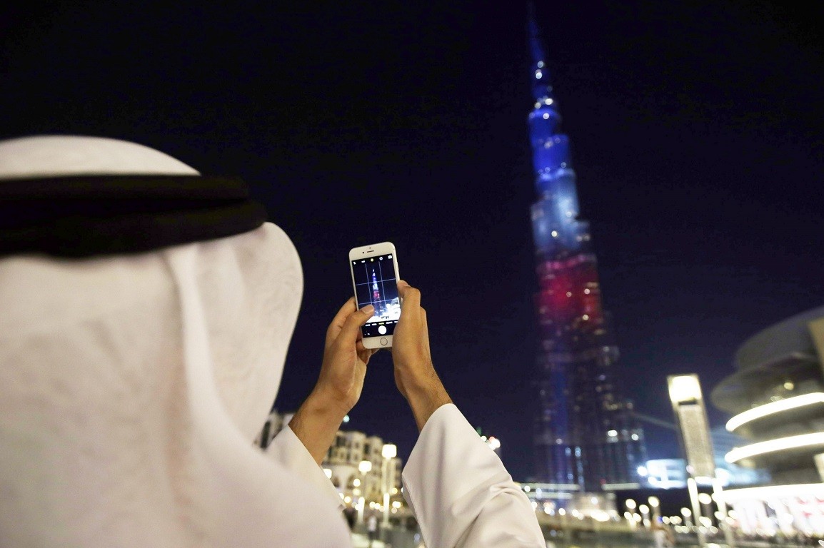 epaselect epa05027298 A man takes a picture of the World's tallest skyscraper Burj Khalifa, which is illuminated in the colours of the French flag in order to show solidarity after the Paris terror attacks of 13 November, in the Gulf emirate of Dubai, United Arab Emirates, 15 November 2015. At least 132 people were killed and some 350 injured in the terror attacks which targeted the Bataclan concert hall, the Stade de France national sports stadium, and several restaurants and bars in the French capital. Authorities believe that three coordinated teams of terrorists armed with rifles and explosive vests carried out the attacks, which the Islamic State (IS) extremist group has claimed responsibility for.  EPA/ALI HAIDER